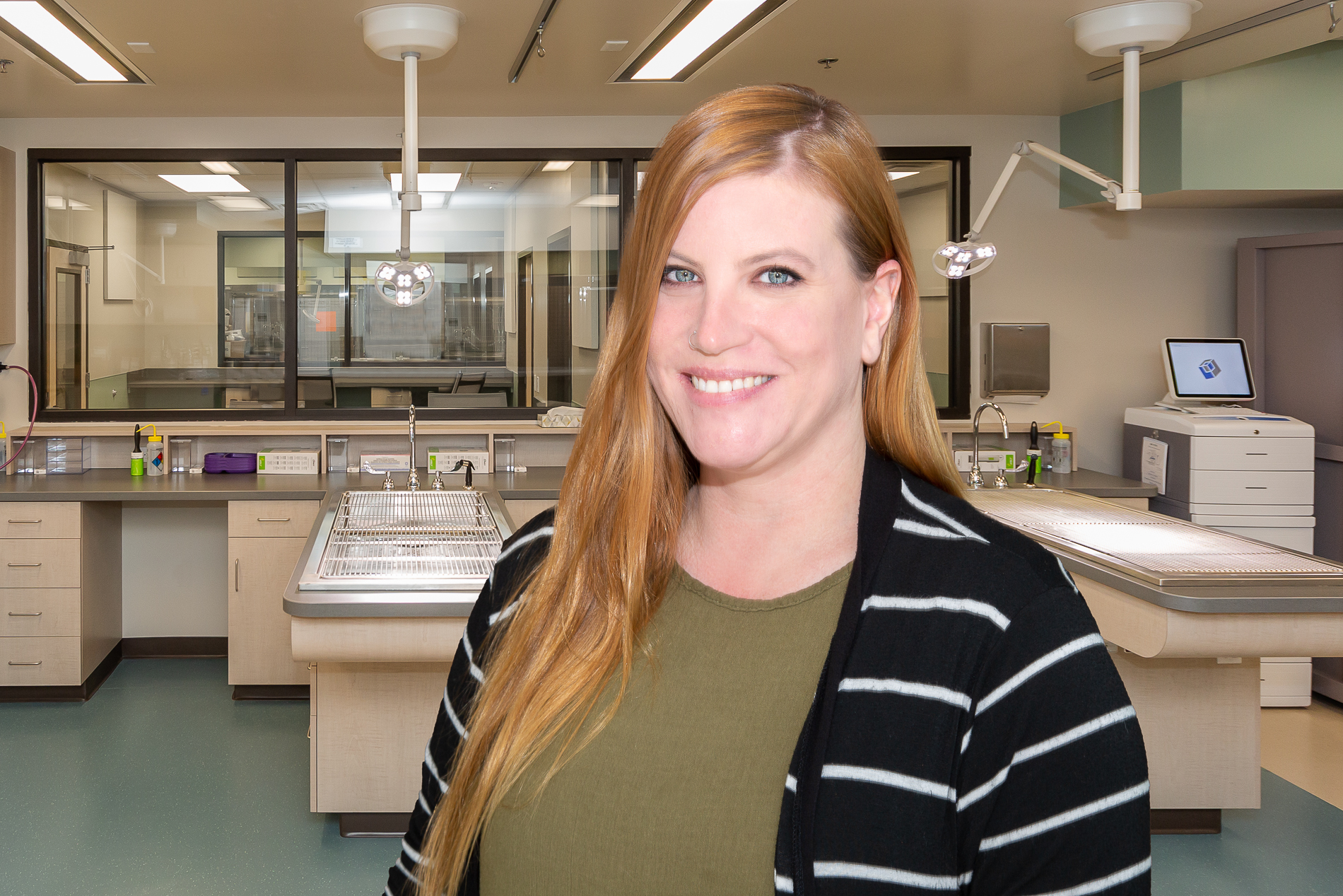 Heather Papa A woman with long blond hair, wearing a black and white striped cardigan over a green shirt, smiles at the camera. She is standing in a modern laboratory with various equipment, including tables, lights, and a computer workstation in the background.